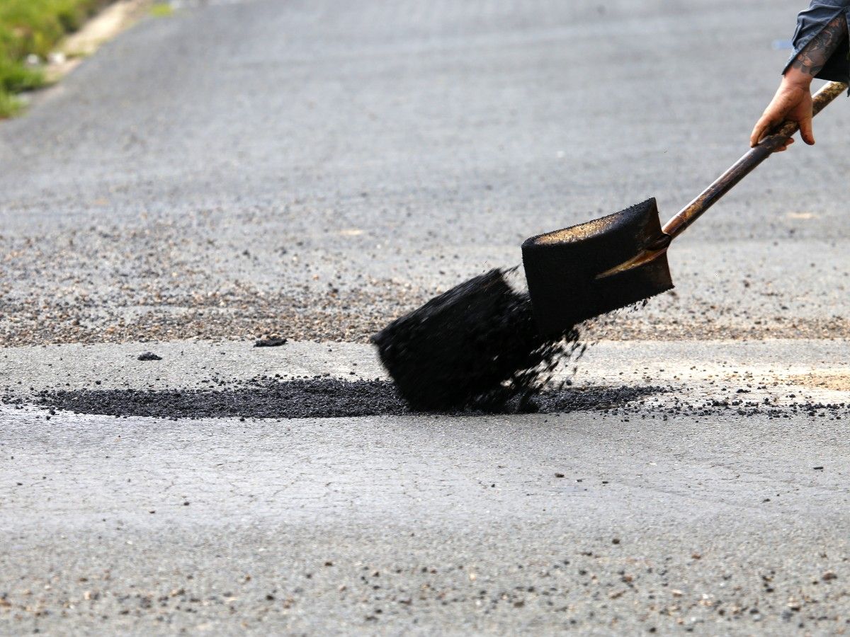 Road crew shovelling bitumen into pothole in suburban area