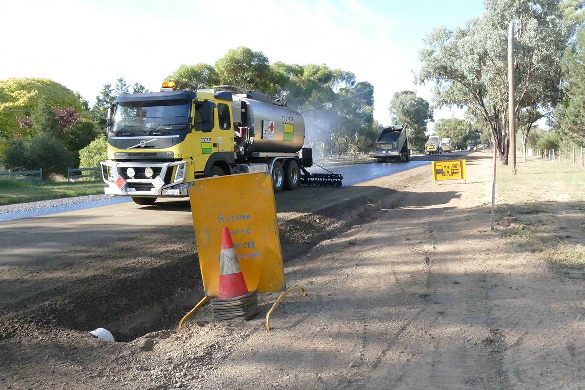 Bitumen sealing truck spraying seal, with gravel trucks in background