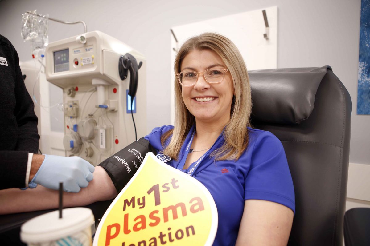 Executive Assistant to the Mayor, Cassandra Webster, about to donate plasma , holding a sign which reads 