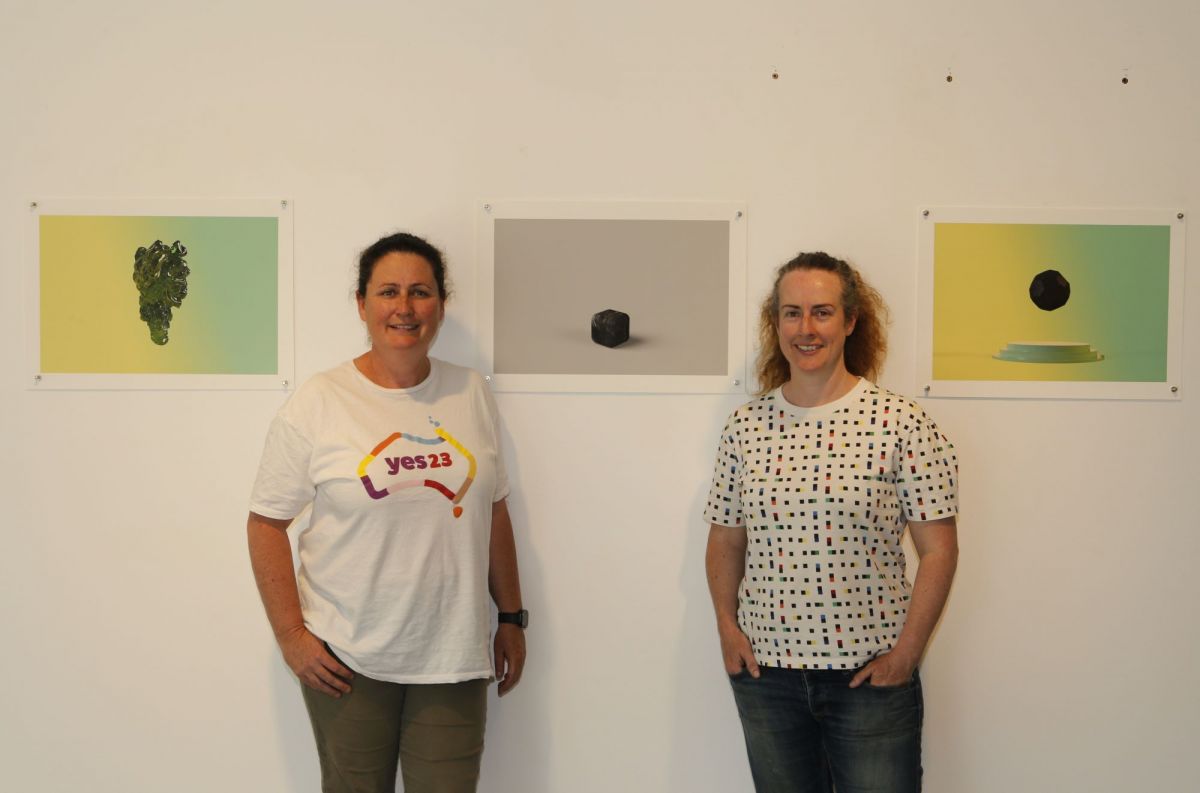 Two women standing amongst their artworks which are pinned to a wall. 