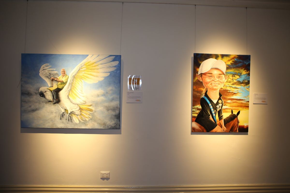 Two satirical portrait paintings on the wall of a gallery. 
