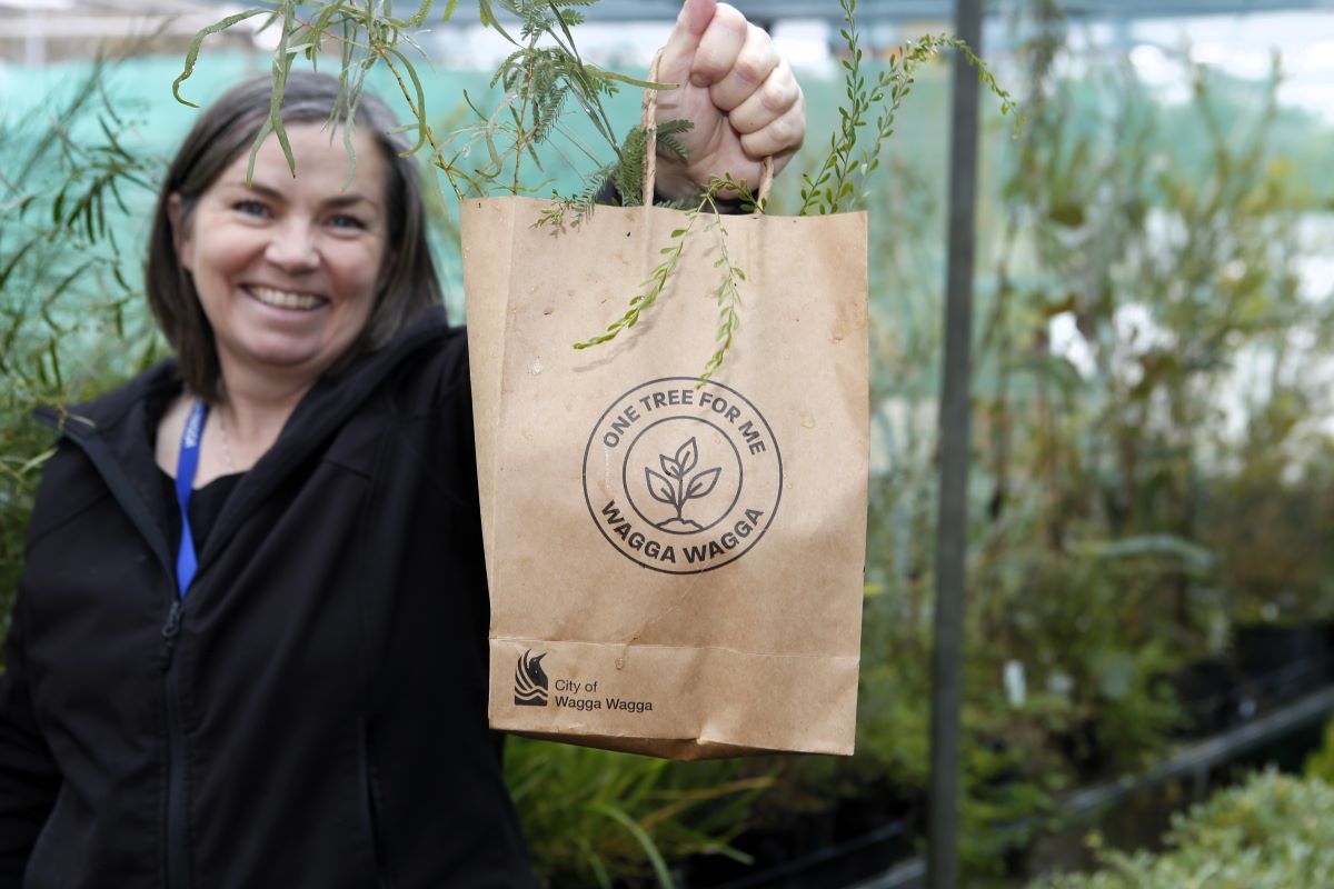 A woman holds a brown paper bag out at the camera. The bag has seedlings in it and the logo on the bag says 