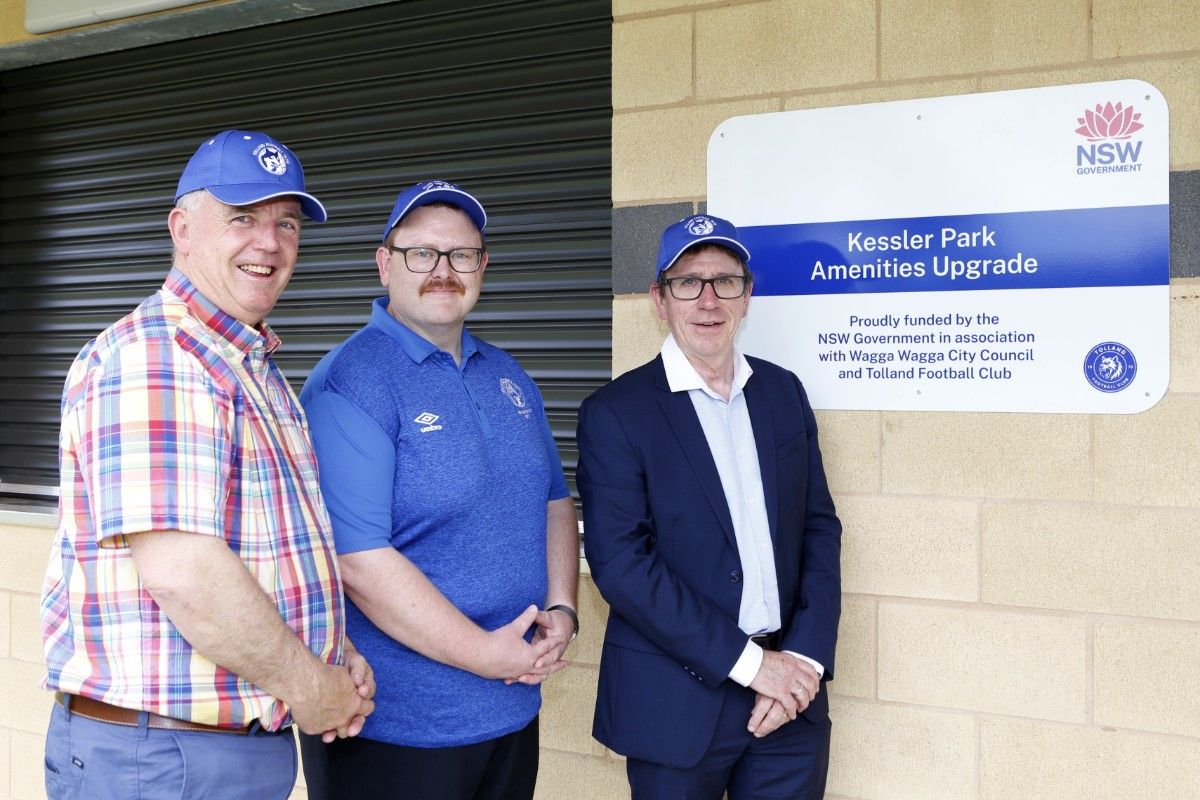 Three men wearing all blue caps with the Tolland Wolves Football Club logo on them stand next to the official funding sign for the upgraded Kessler Park amenities building.