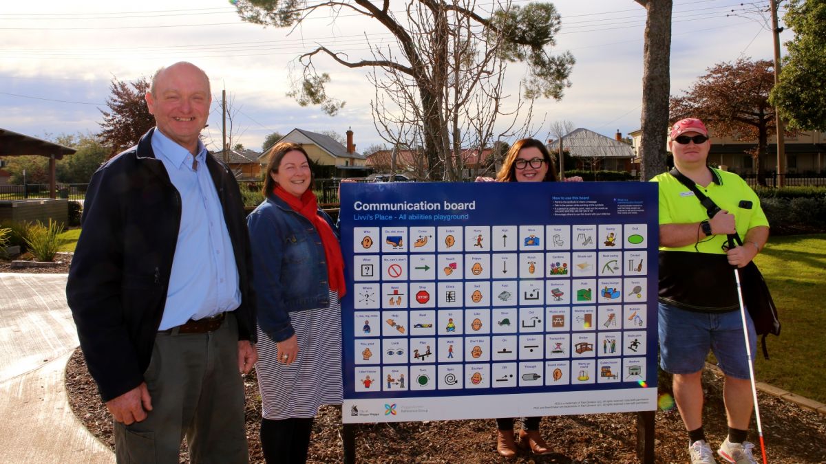 Two men and two women standing around a communication board