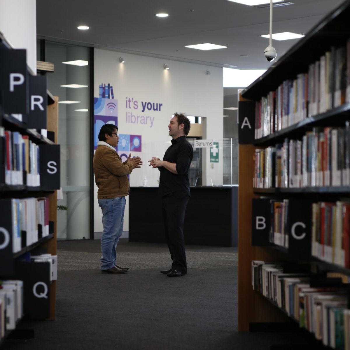 Two men standing at end of aisle of books at library