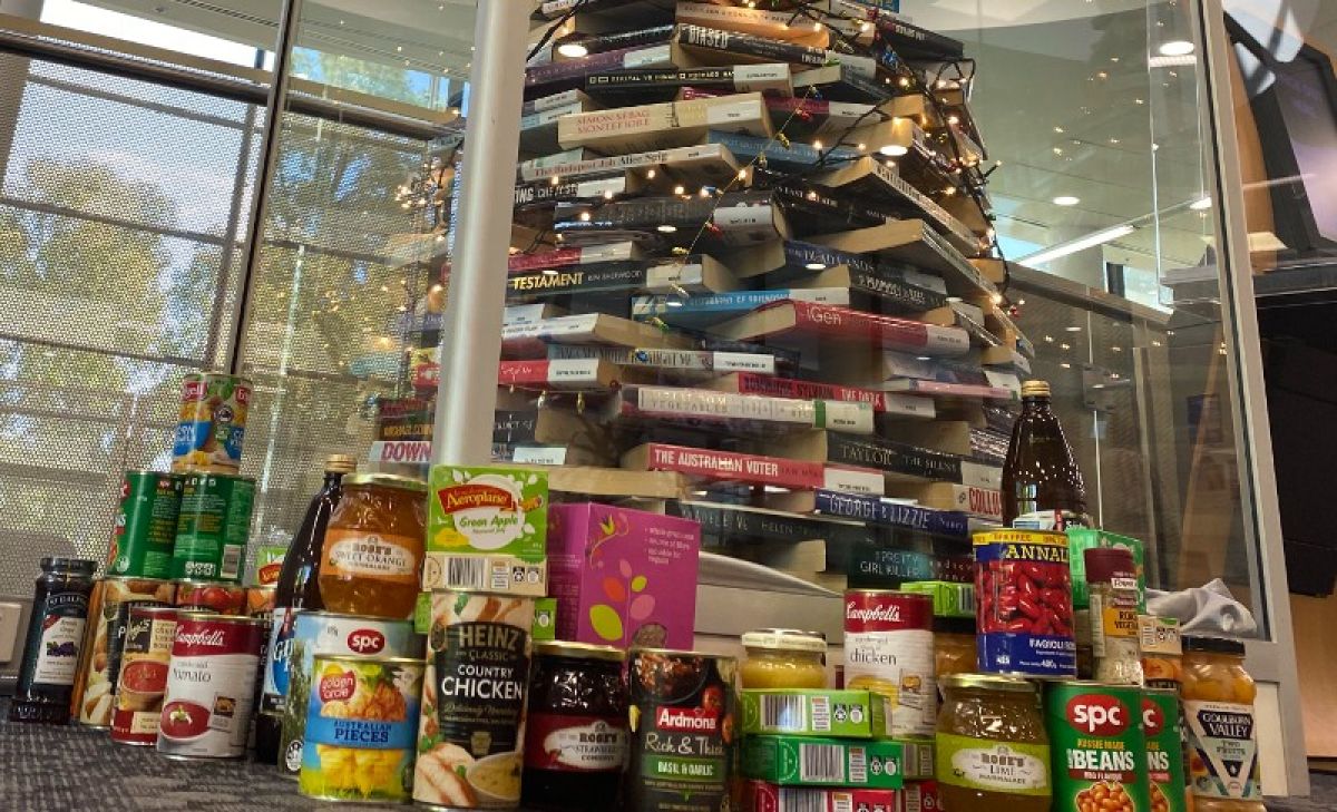 Canned of food at the base of a Christmas tree made from books