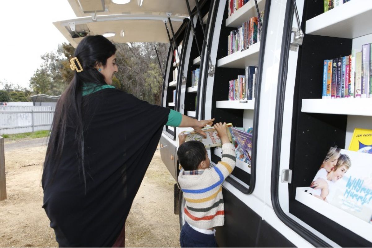 A woman helps a young boy choose a book from a van filled with books