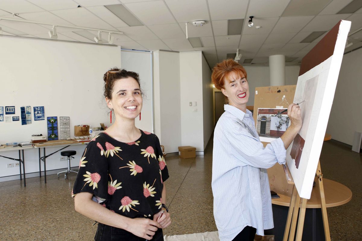 Two woman standing next to art canvas in gallery space