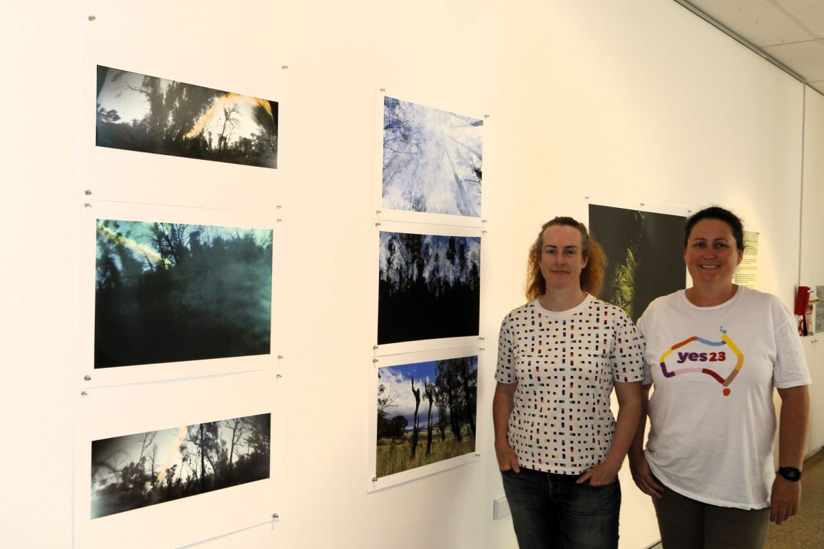 Two women standing alongside a wall with photographs of landscapes.
