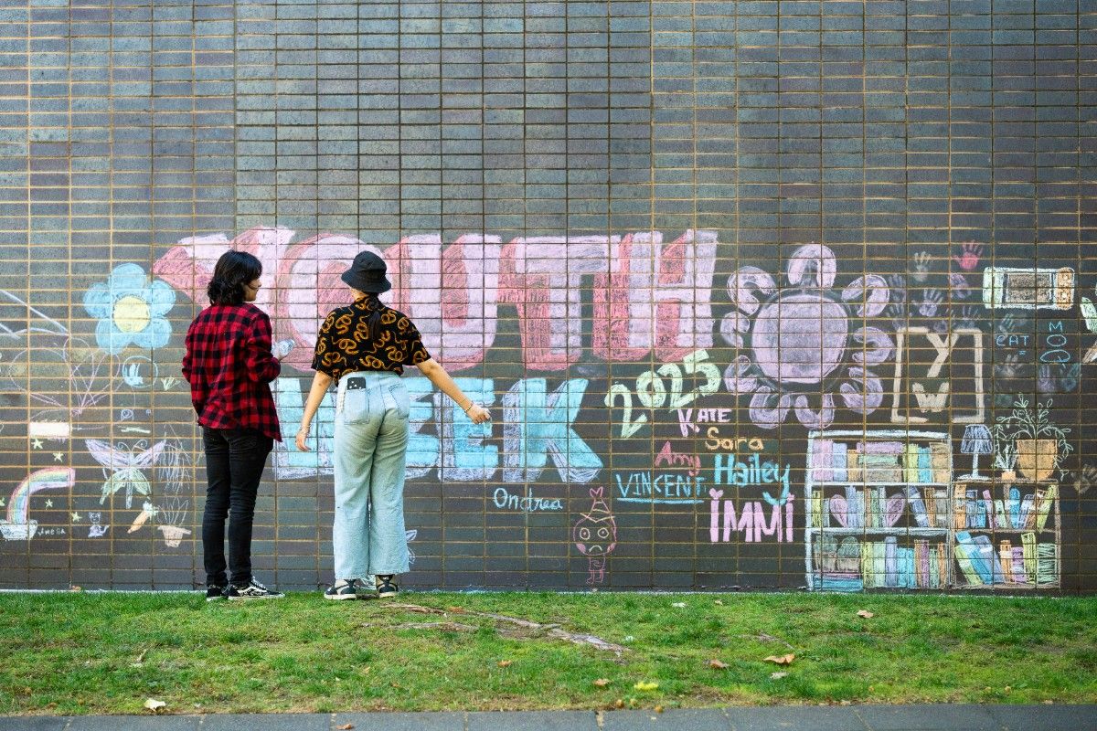 Back view of two young people creating chalk mural on a brick wall.