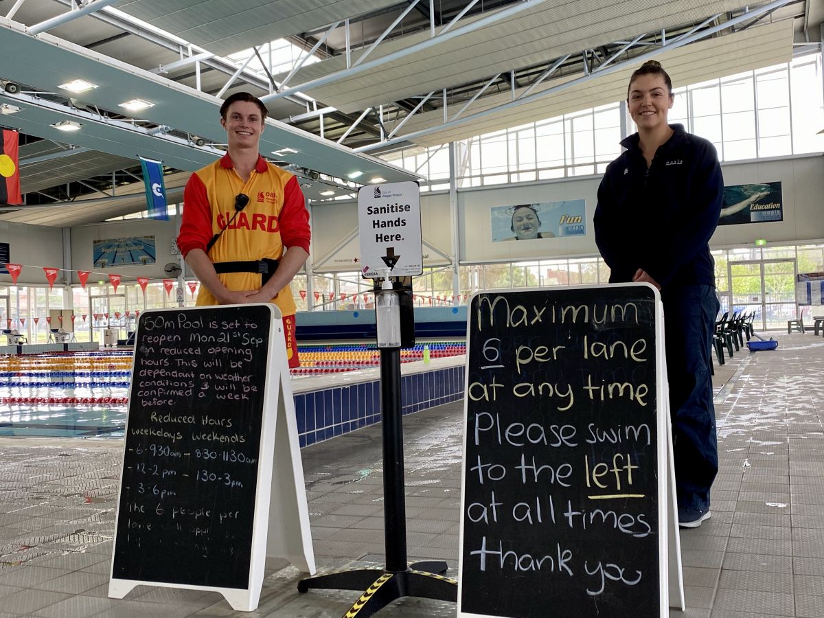 Male pool lifeguard and female Oasis Programs supervisor standing behind signs detailing number of swimmers per lane