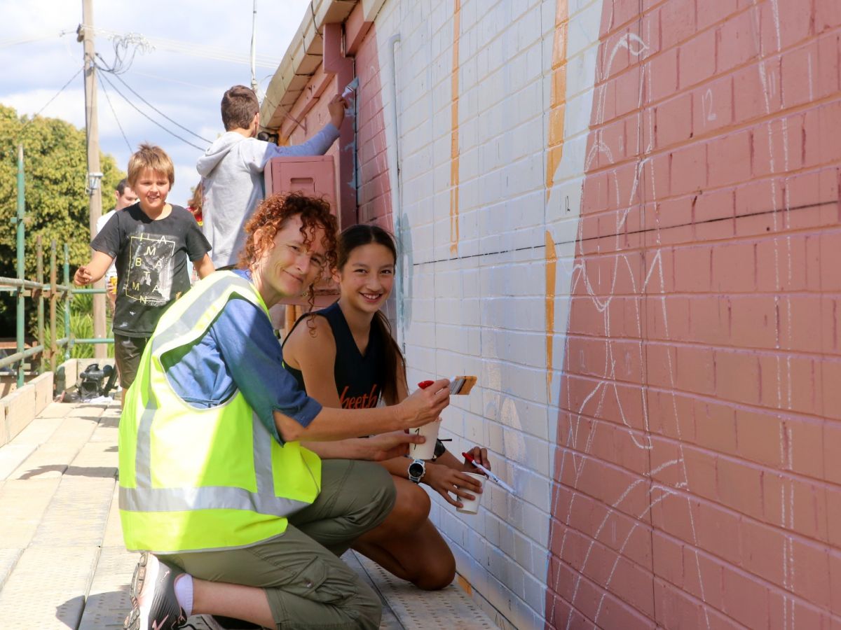 Woman in flouro vest and young woman painting wall with other young people in background