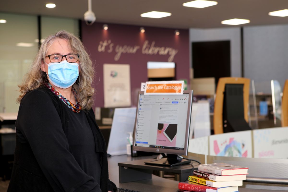 Woman standing next to computer and pile of books in library