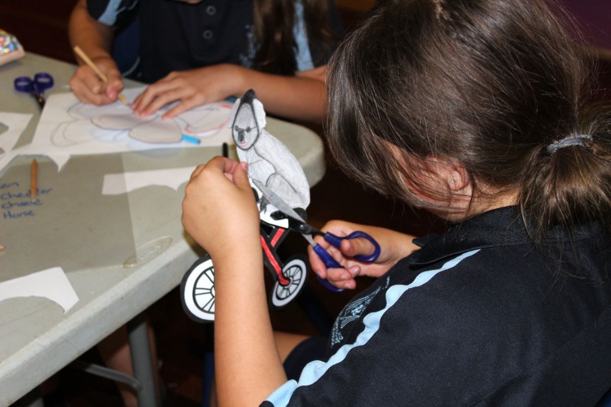 A young student cutting around a drawing of a koala riding a bicycle