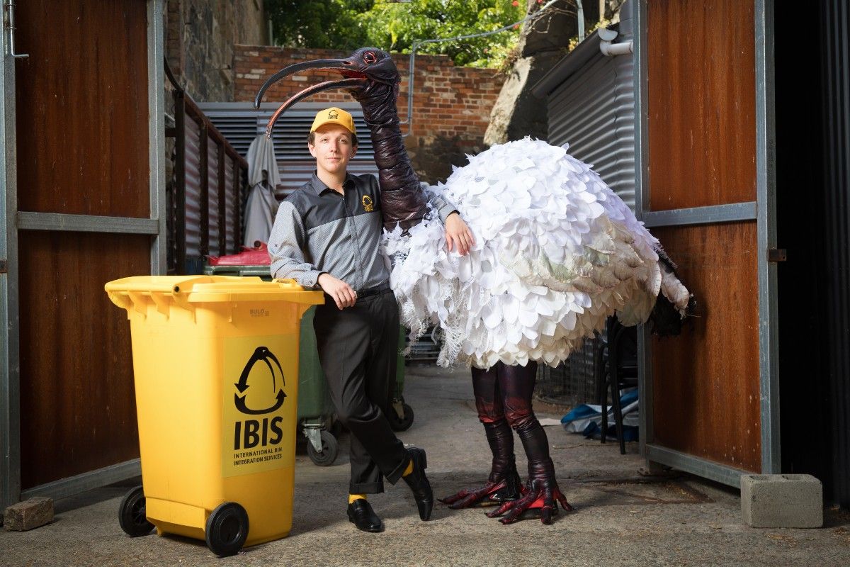 Man leaning on recycling bin with man in ibis suit