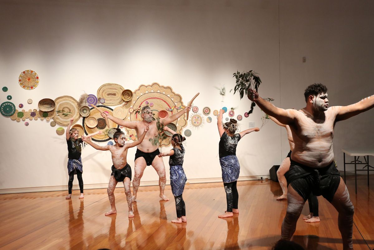 Two men and four children dance in a gallery setting