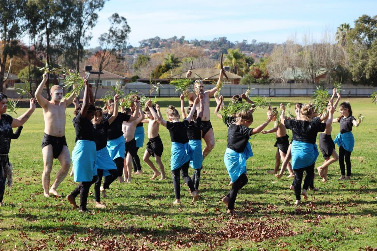 Young First Nations people dancing in a field holding gum leaves. 