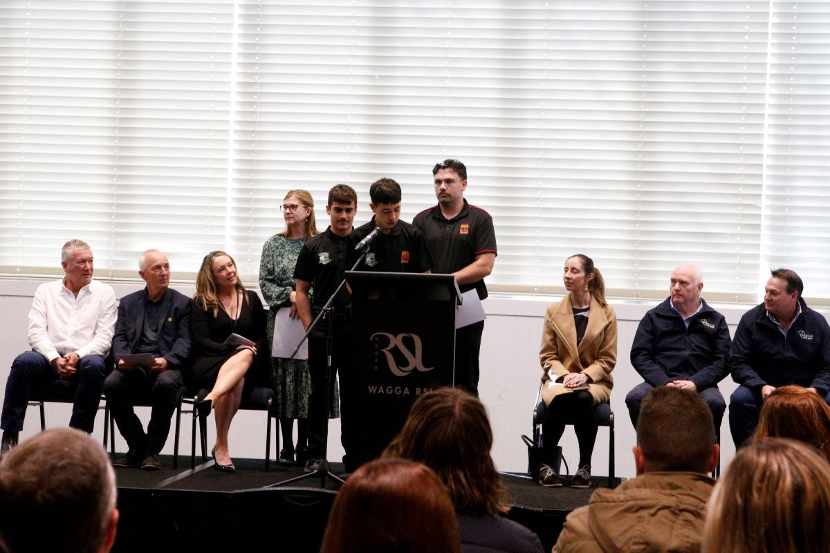 A young man speaks to a crowd from a stage behind a lectern. 