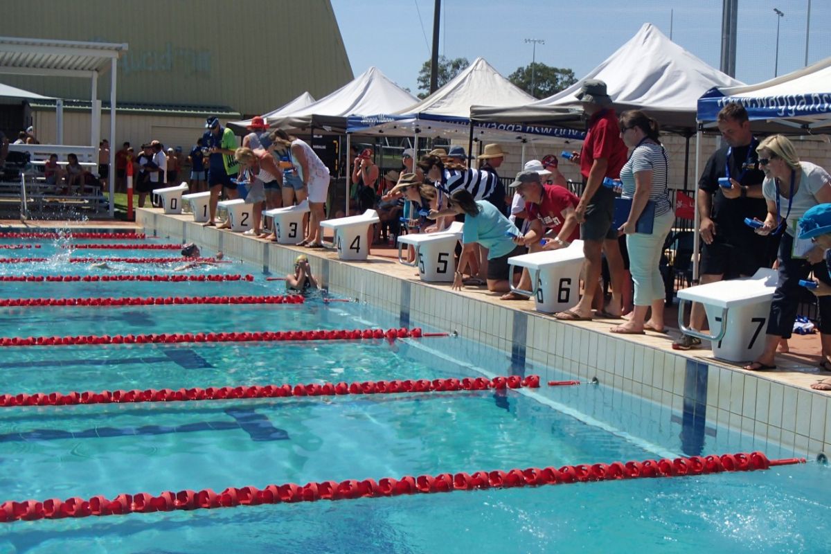 Junior swimmers and officials near the starting block of outdoor Olympic swimming pool.