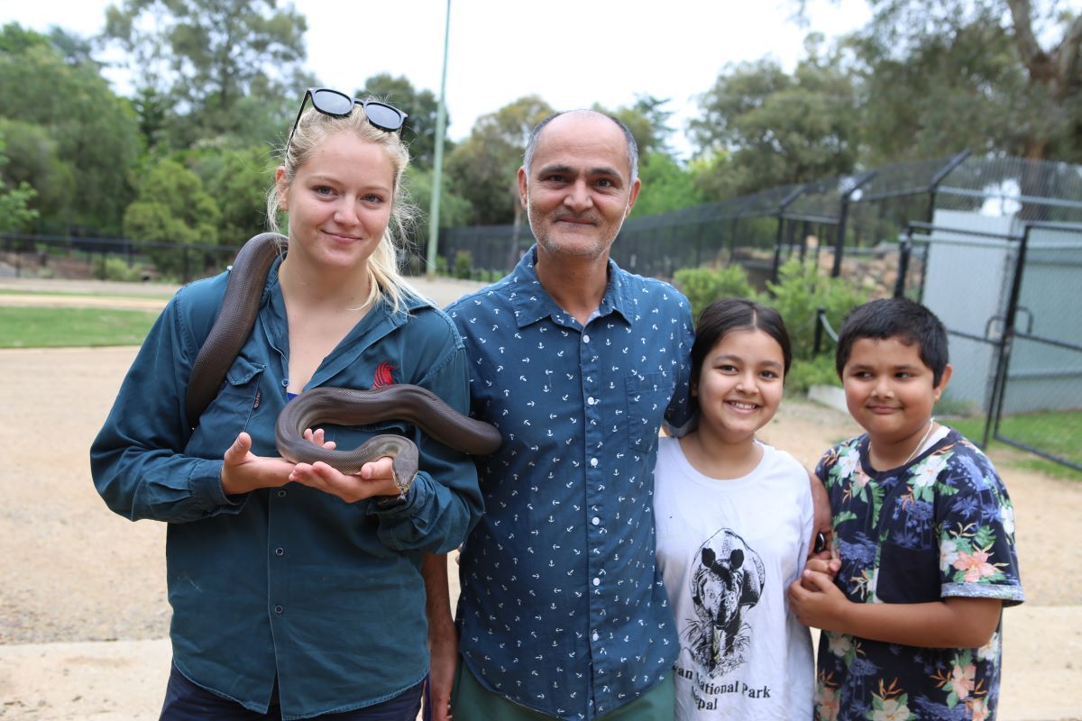 A young woman holding a large brown python standing next to a man and two children
