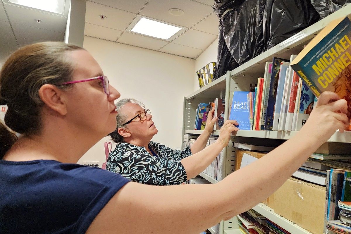 Two women standing side by side, putting books on shelves