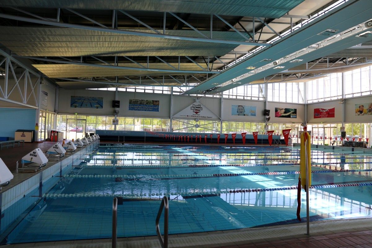 Indoor large swimming pool, with starting blocks and lane ropes in a building with lots of glass windows.