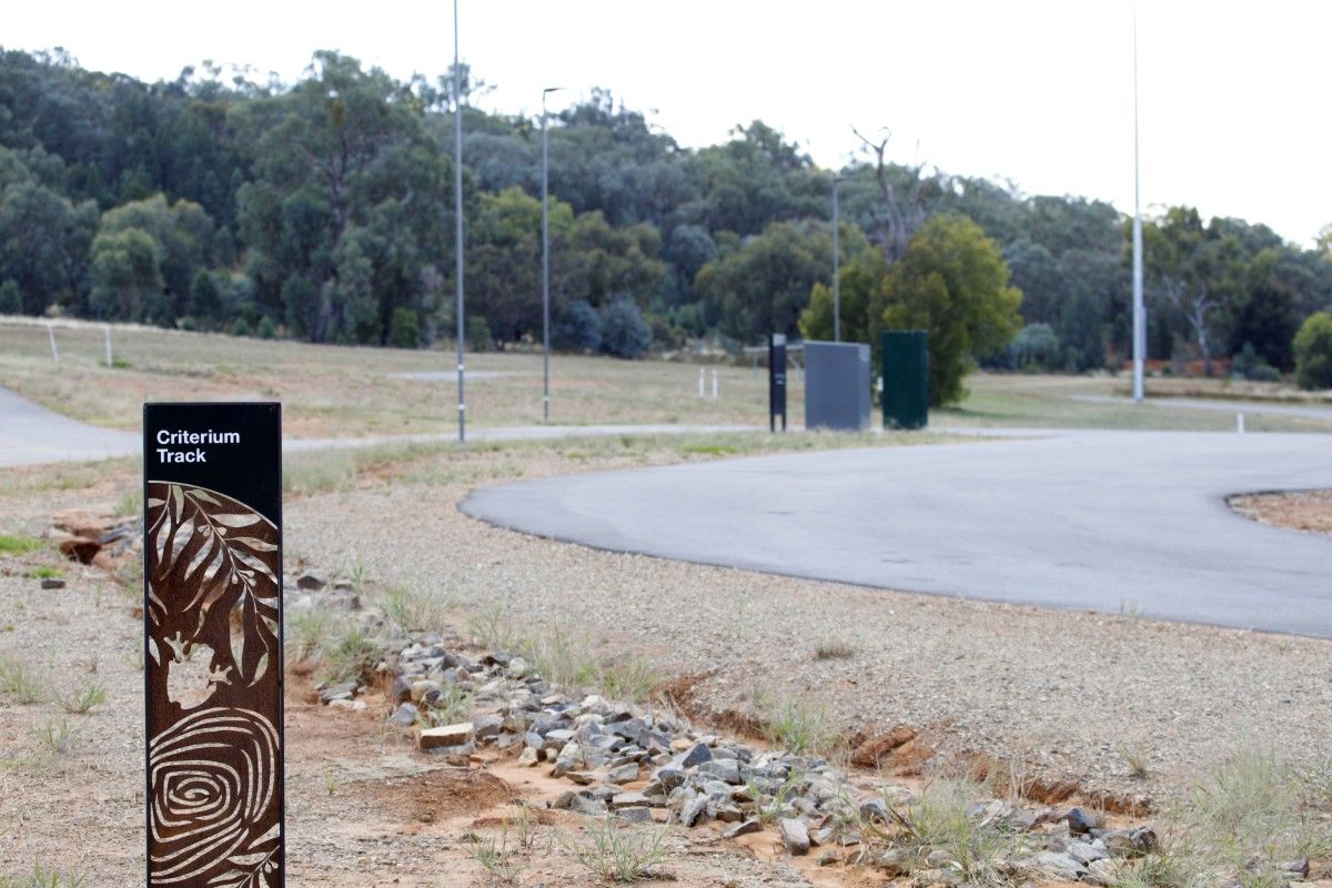Metal sculpture sign saying criterium track with curved section of the asphalt track on right hand side of sign.